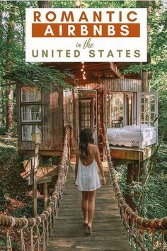 a woman walking across a wooden bridge in the middle of a forest with a small cabin behind her