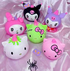 five hello kitty stuffed animals are on a pink satin surface, one is wearing a bow and the other has a spider