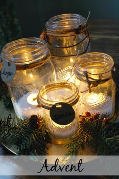 mason jars filled with candles on top of a table next to evergreen branches and pine cones