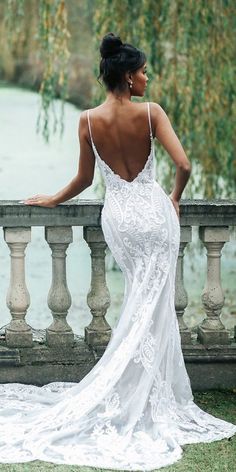 a woman in a white wedding dress standing on a balcony looking at the water and trees