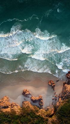 an aerial view of the ocean with waves coming in from the shore and rocks on the beach