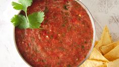 a bowl of salsa with tortilla chips and cilantro on the side