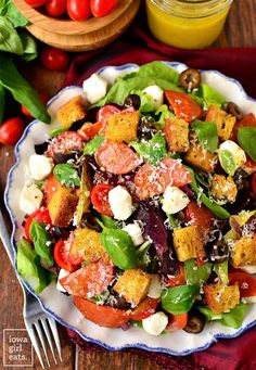 a salad with tomatoes, mozzarella and olives on a plate next to a glass of orange juice