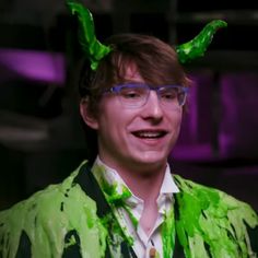 a man with green paint on his face wearing glasses and a shirt that has horns