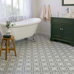 a white bath tub sitting next to a wooden stool in a bathroom under a window