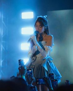 a woman in white dress standing on stage with microphone and cell phone to her ear