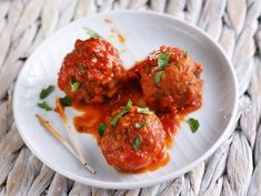 three meatballs covered in marinara sauce and garnished with parsley on a white plate