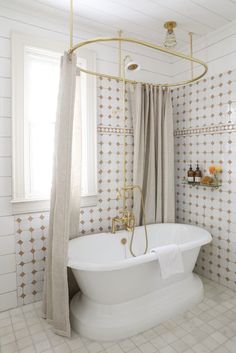 a white bath tub sitting under a window next to a curtained shower stall with gold fixtures