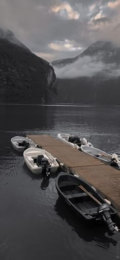 several small boats are docked at the end of a pier on a lake with mountains in the background