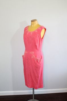 "The most perfect and prettiest 1950s pink wiggle dress! It features beautiful lace at the neck, two huge pockets in front, studs in floral patterns, and rhinestones. FEATURES: * Label: None * Circa: 1950s * Materials: Unmarked. Feels like a woven cotton, possibly with some rayon * Color: Pink (almost a salmon, but more pink) * Pattern: Floral stud pattern * Length: Below knee * Waist: Fitted natural waist * Sleeves: Sleeveless * Neckline: Scoop * Closure: Metal zipper up the back with hook and Pink Fitted Dress With Pockets, Pink Fitted Dresses With Pockets, Fitted Pink Dresses With Pockets, Pink Sleeveless Dress For Vintage Fashion, Pink Fitted Vintage Dress, Funky Dresses, Floral Studs, Pink Pattern, Wiggle Dress