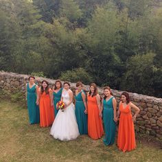 a group of women standing next to each other in front of a stone wall and trees