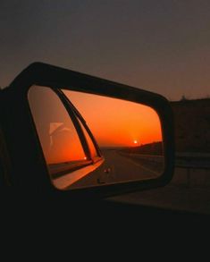 the sun is setting in the distance as seen from a car's rear view mirror