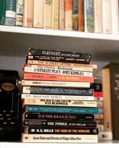 a stack of books sitting on top of a white book shelf next to a typewriter