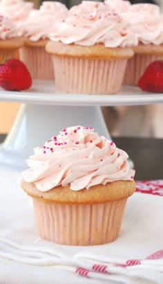 two cupcakes with pink frosting and sprinkles are on a cake stand