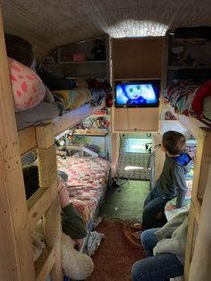 two children sitting on bunk beds in a small room with a television and other items