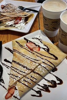 two plates with pancakes and strawberries on them, one has whipped cream and the other has chocolate syrup