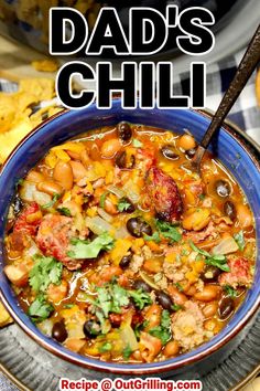 a blue bowl filled with chili and beans next to tortilla chips on a plate