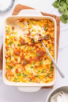 a casserole dish with cheese and vegetables in it on a napkin next to a bowl of sour cream