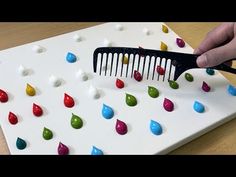 a person is using a comb to cut out candy drops on a white board with black handles