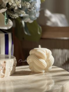 a close up of a white object on a table near a vase with flowers in it