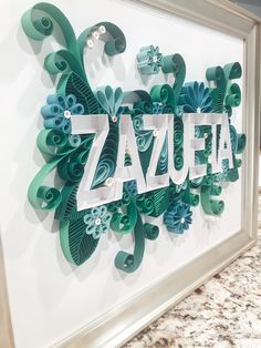 the word zazuta is cut out of paper and placed on a wall in front of a marble countertop