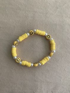 a yellow beaded bracelet with smiley faces and pearls on the end is sitting on a gray surface