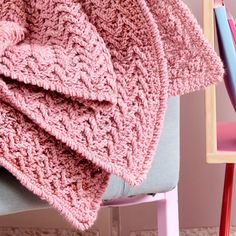 a pink crocheted blanket sitting on top of a chair next to a blue chair