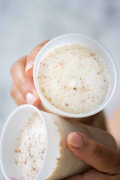 two people holding cups with liquid in them, one is white and the other has brown flecks on it