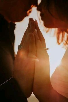 two people holding their hands together with the sun shining behind them and they are touching each other