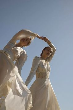 two women in white dresses standing next to each other with their hands on their head