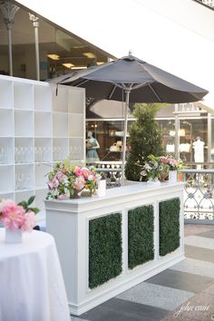 an outdoor bar with plants and flowers on the outside wall, next to a white table