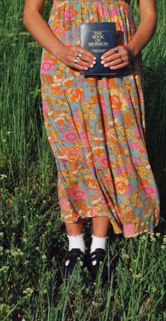 a woman standing in the grass holding a book