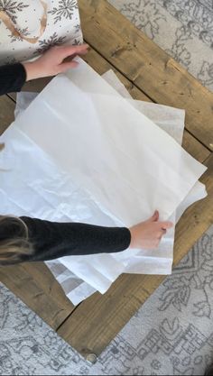 a person holding some white paper on top of a wooden table next to a bag