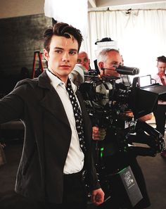 a man in a suit and tie standing next to a cameraman holding a video camera