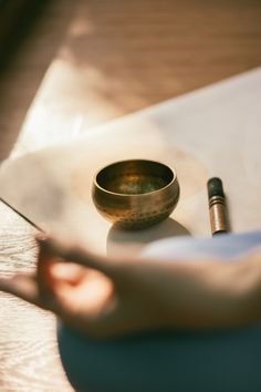 a person's hand holding a pen over a paper with a bowl on it