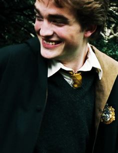 a young man wearing a harry potter sweater and smiling at someone in front of some trees