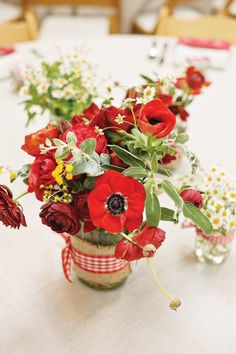 red flowers are arranged in vases on a white table cloth covered dining room table