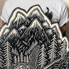 a man wearing a white t - shirt with an image of mountains and trees on it