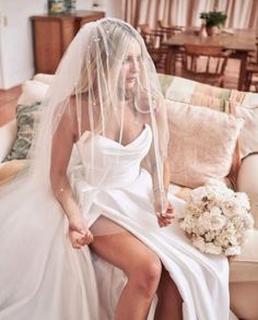 a woman in a wedding dress sitting on a couch with her veil over her head