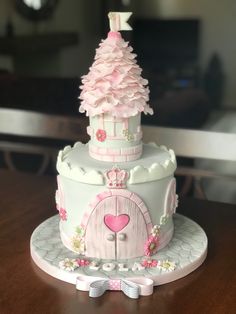 a pink and white cake with a tree on top is sitting on a wooden table