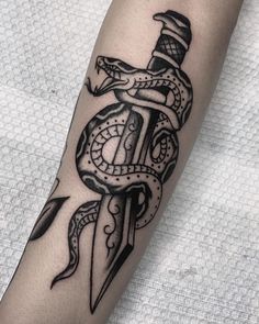 a black and white tattoo on the arm of a person with a dagger, snake and anchor