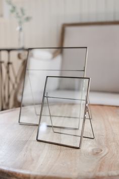 two glass frames sitting on top of a wooden table next to a white vase and chair