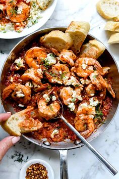 a pan filled with shrimp and bread on top of a white marble counter next to garlic bread