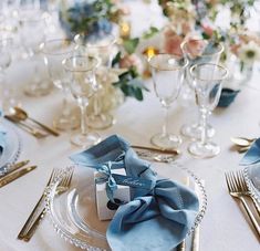 the table is set with blue napkins and silverware, gold cutlery, and floral centerpieces