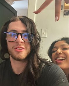 a man with long hair and glasses standing next to a woman in front of a mirror