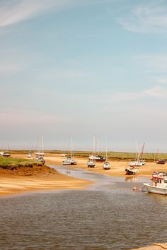 several boats are docked on the shore near the water's edge, with sand and grass in the foreground