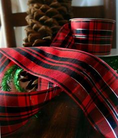 a red and black plaid ribbon on a wooden table with pine cones in the background