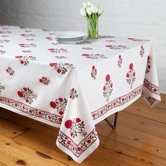 a white table topped with a vase filled with flowers next to a plate on top of a wooden floor