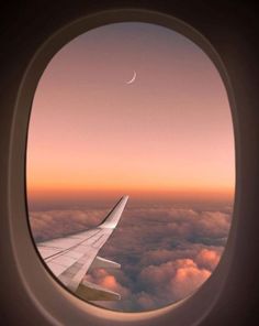 an airplane window with the view of clouds and a crescent in the sky at sunset