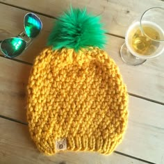 a yellow knitted hat with green pom - pom sitting next to sunglasses